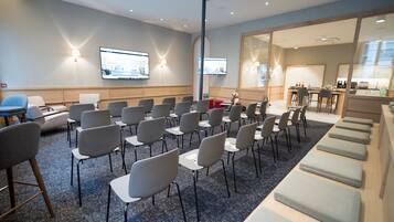 Un salón de conferencias con filas de sillas, una pantalla grande y una zona de kitchenette.