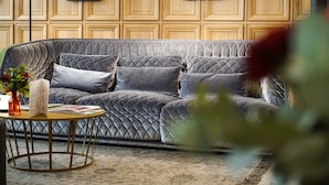 Una sala de estar moderna con un sofá gris acolchado, una mesa redonda con marco dorado y una pared de paneles de madera con cuadros.