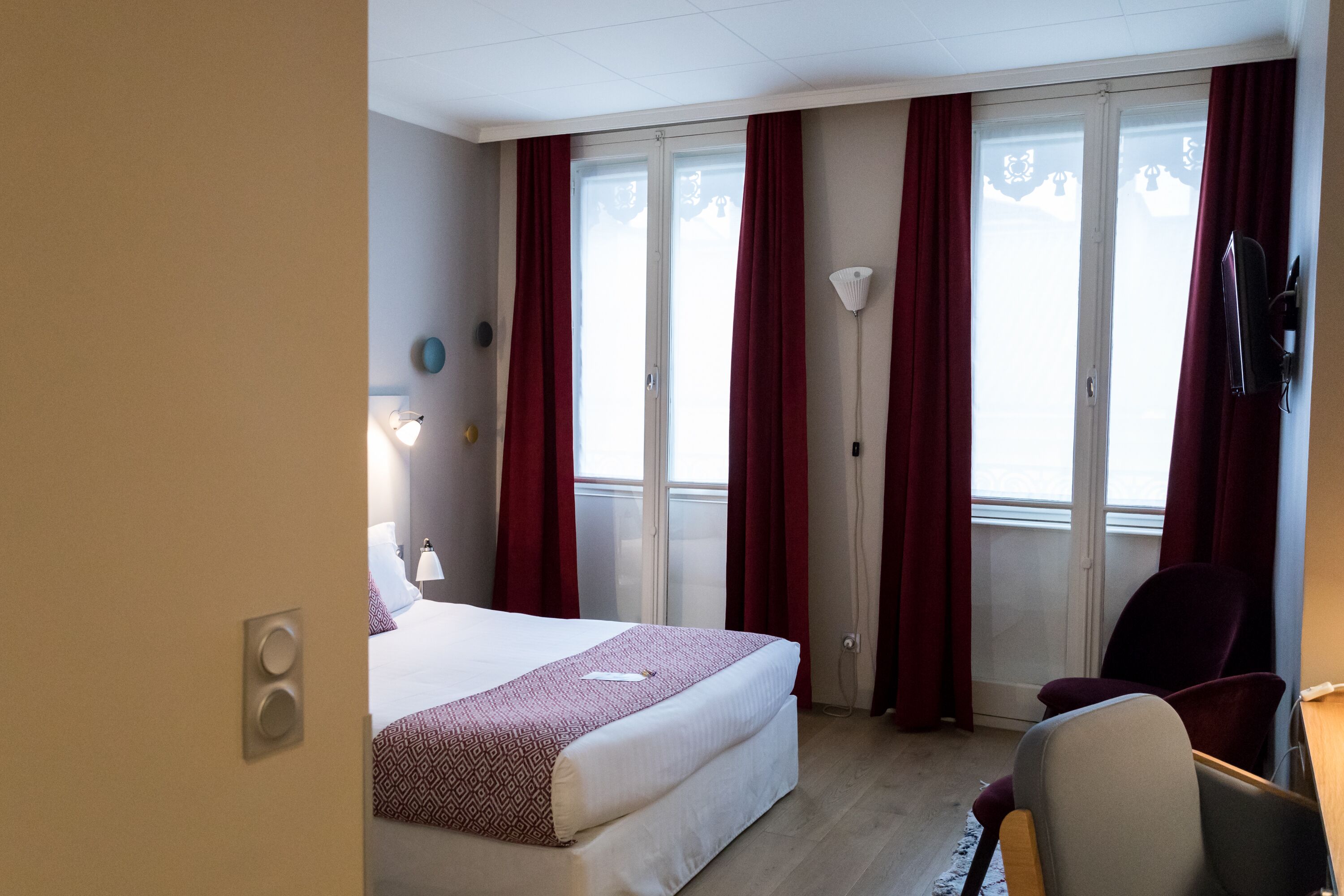 Een hotelkamer met een bed, een bureau, een stoel, een televisie en een raam met gordijnen.