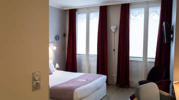 A hotel room with a bed, a desk, a chair, a TV, and a window with curtains.