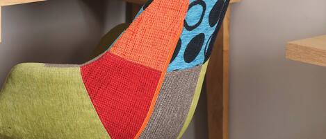 A chair with a colorful patchwork backrest and a wooden desk with a framed certificate or document.