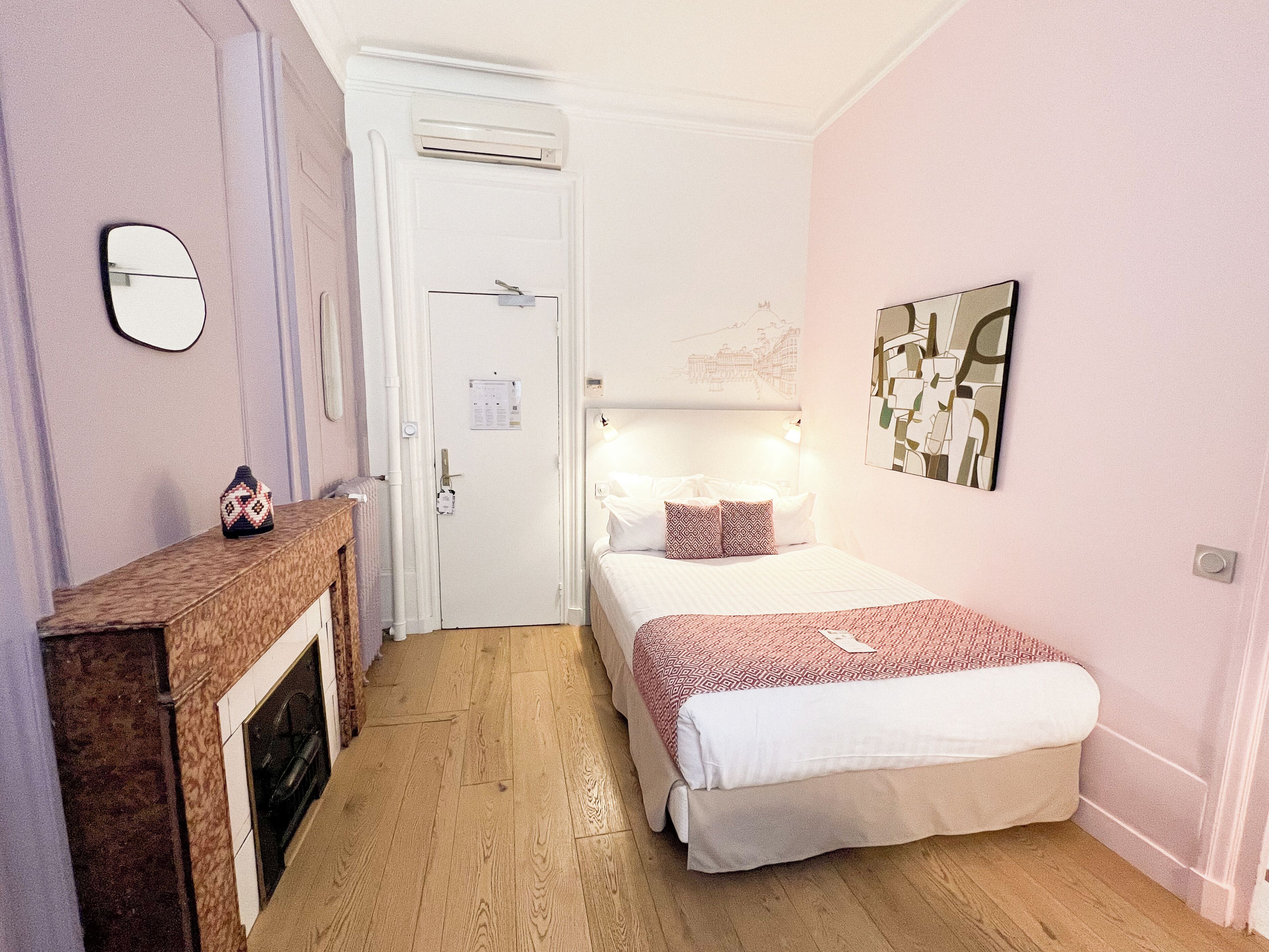 A bedroom with a bed, a bedside table, a mirror, a fireplace, and a wall-mounted artwork.