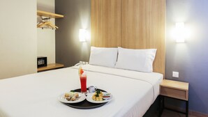 Habitación de hotel con una cama bien hecha, una bandeja con alimentos para el desayuno, una mesita de noche y un aplique de pared.