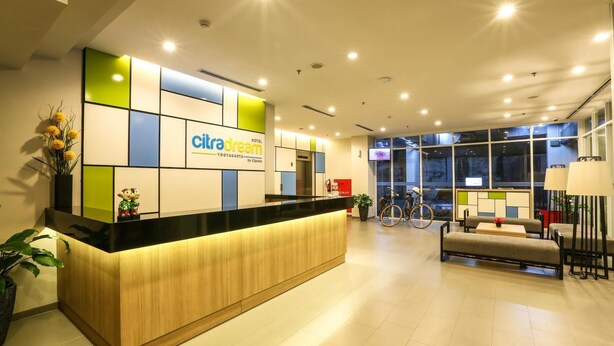 Zona de recepción de hotel con diseño moderno, que incluye mostrador de recepción, área de descanso y ventanas amplias.