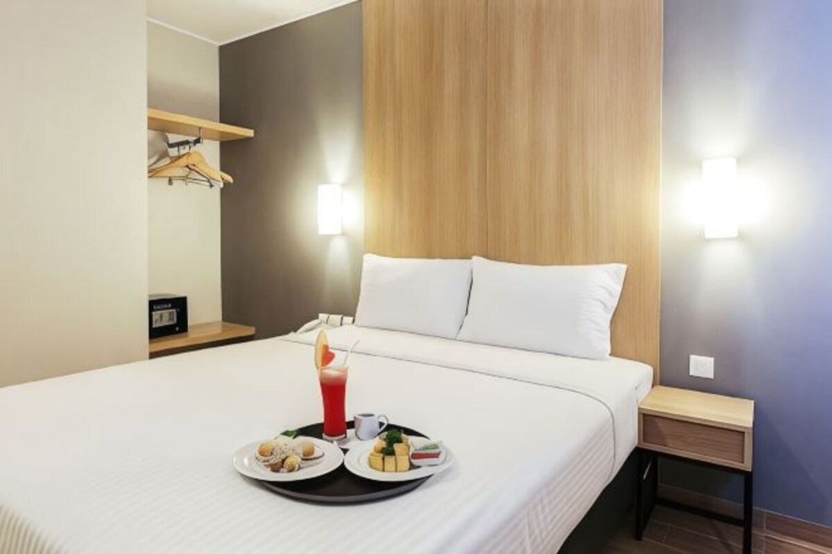 Habitación de hotel con cama, mesitas de noche, una bandeja de desayuno y luces en la pared.
