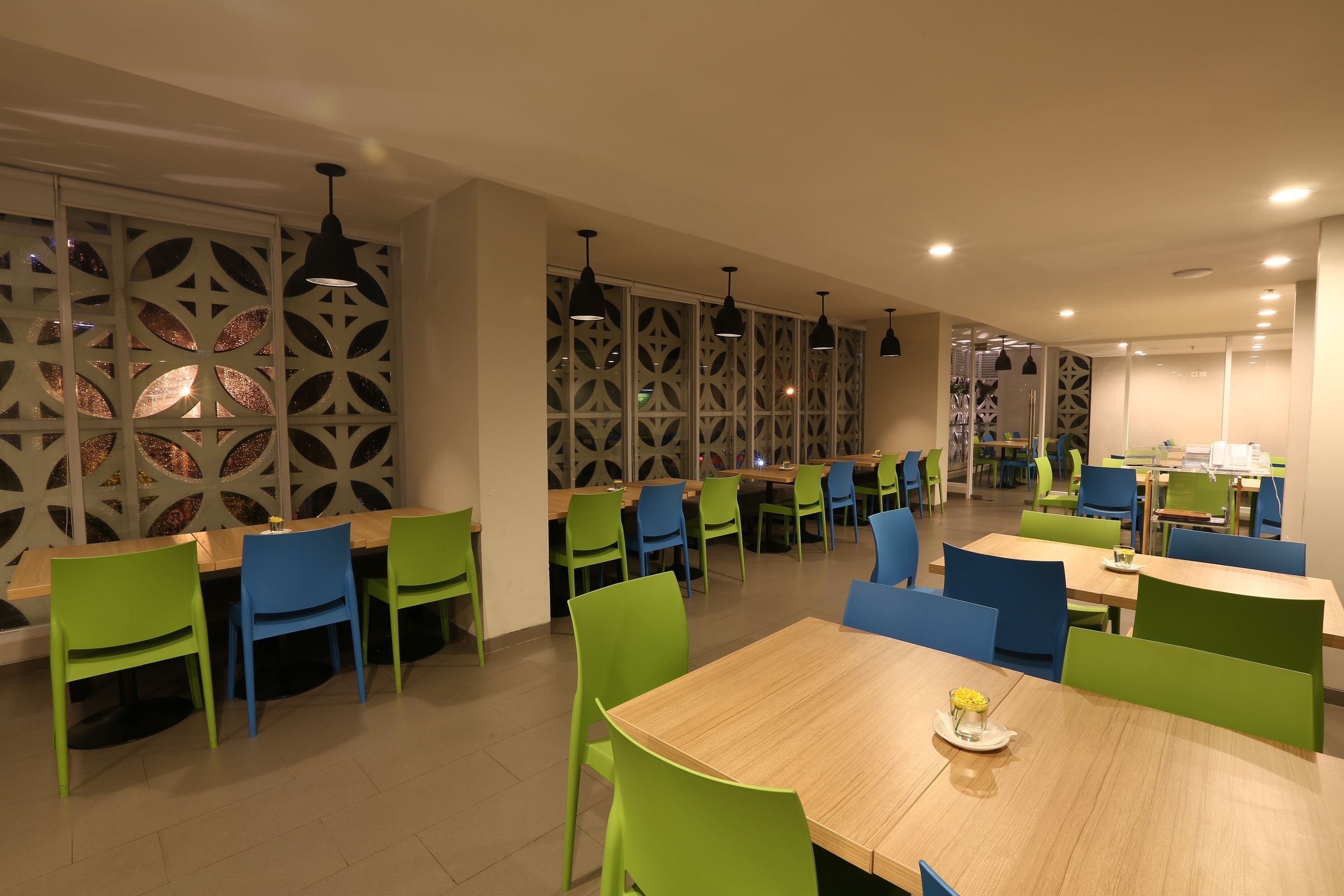 A modern dining area with wooden tables and green and blue chairs, featuring decorative wall panels and pendant lighting.