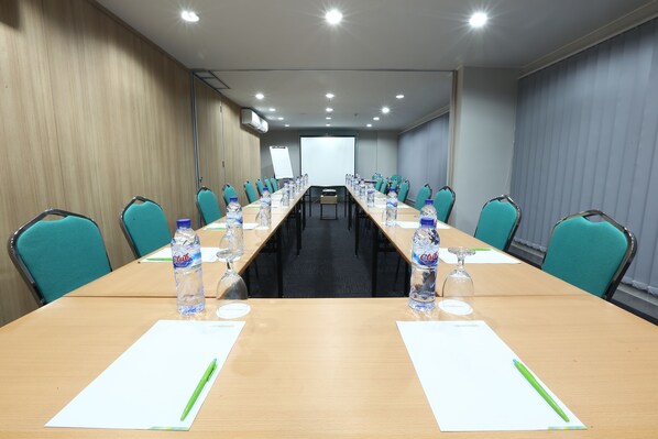 Uma sala de conferência com uma mesa comprida, cadeiras azul-turquesa, garrafas de água e cartões de identificação.