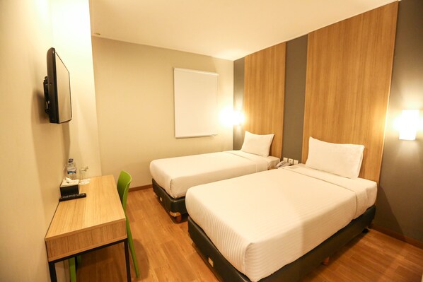 Une chambre d’hôtel avec deux lits simples, un bureau, une chaise, une télévision et une lampe fixée au mur.