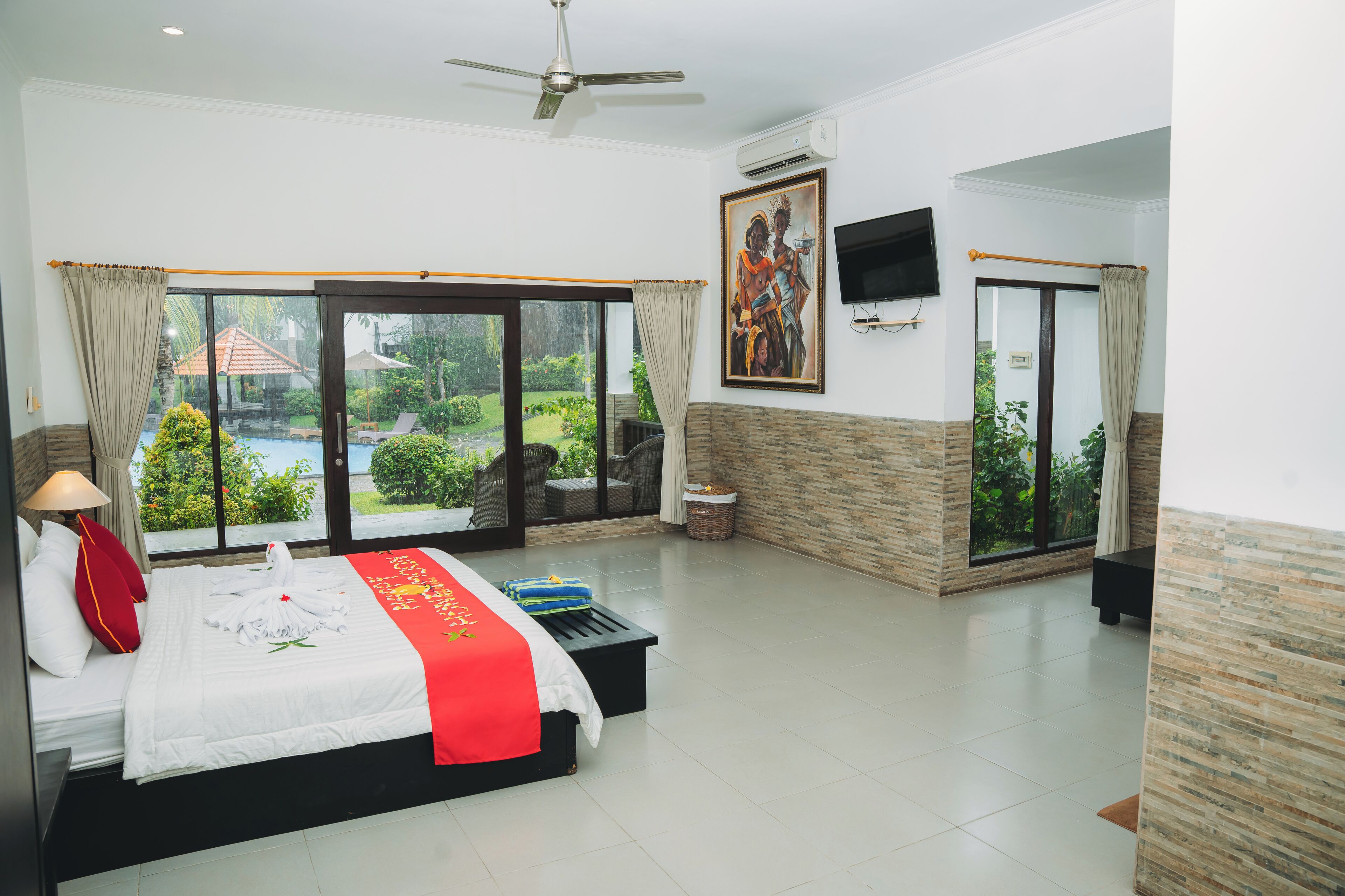 A hotel room with a bed, a ceiling fan, a TV, and a view of the outdoors.