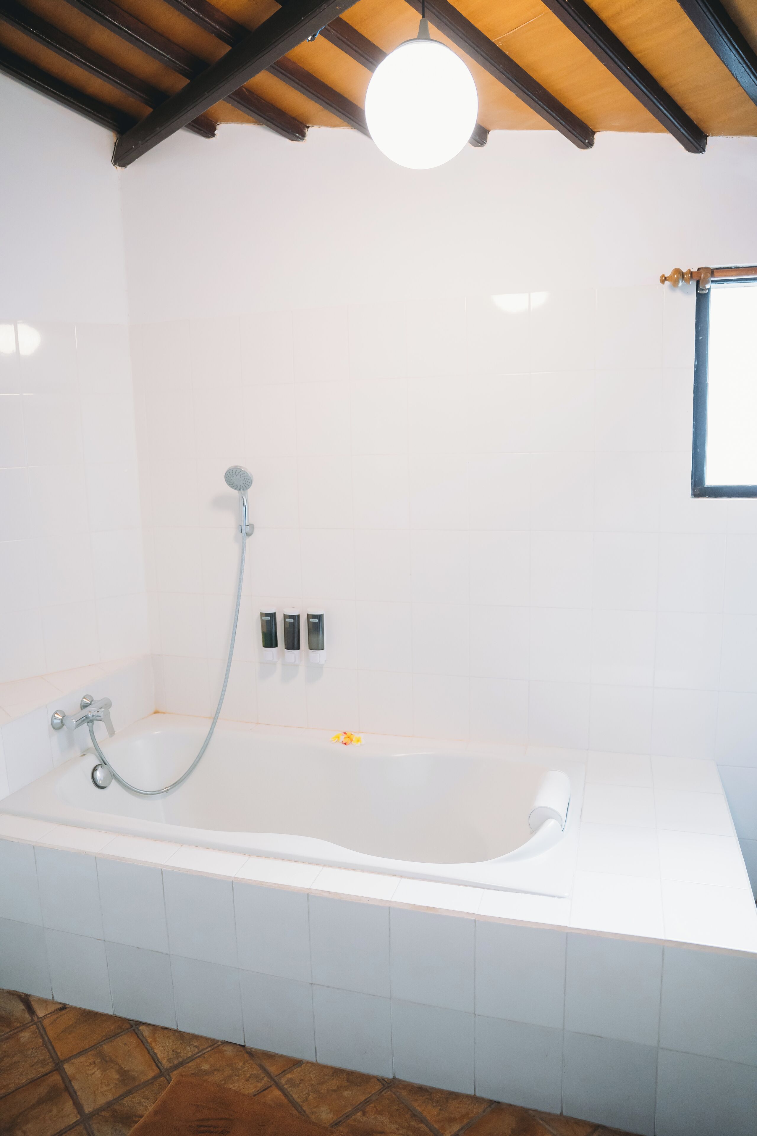 A bathroom with a bathtub, a showerhead, and a window.