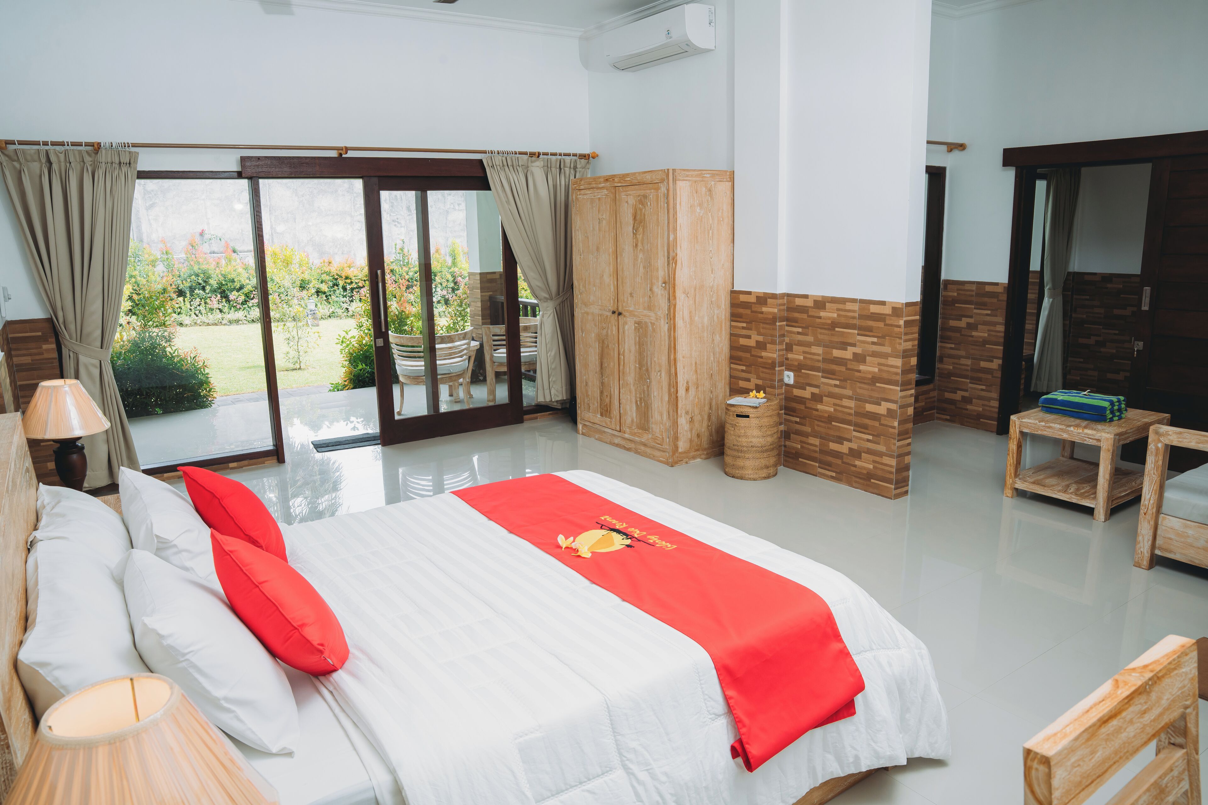 Een hotelkamer met een bed, een houten garderobe, een tafeltje en uitzicht op de tuin door de schuifdeuren.