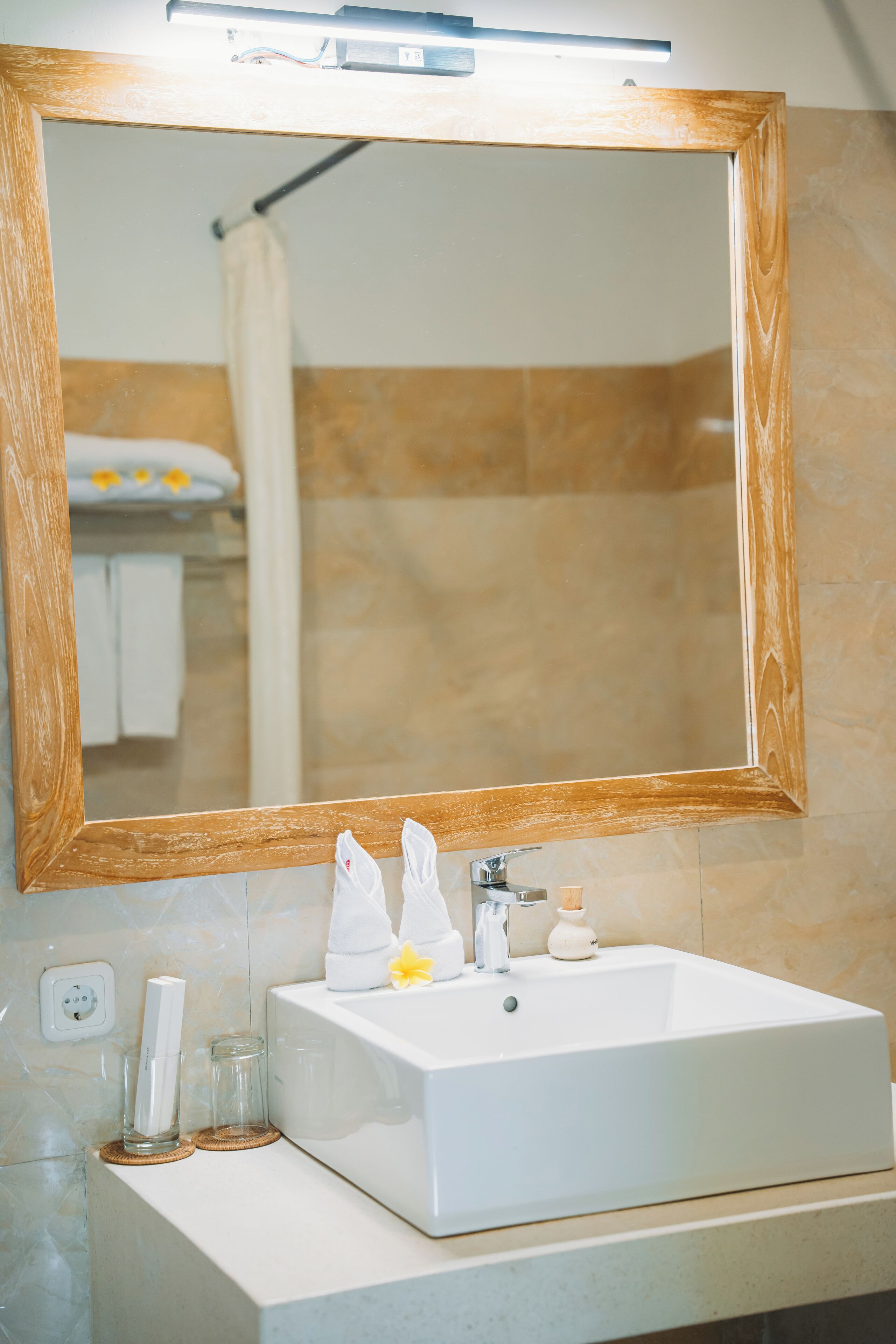 A bathroom with a white sink, a wooden-framed mirror, and a towel hanging on a rack.
