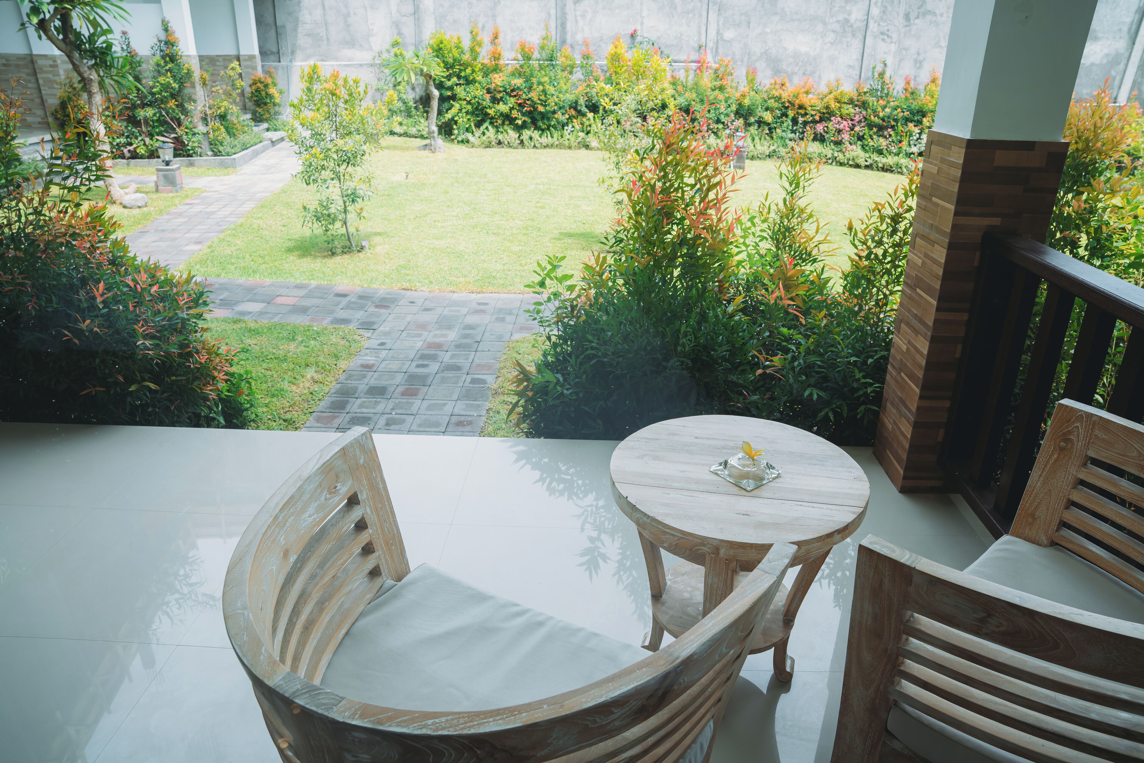 A balcony with a wooden table and chairs, overlooking a garden with various plants and a lawn.
