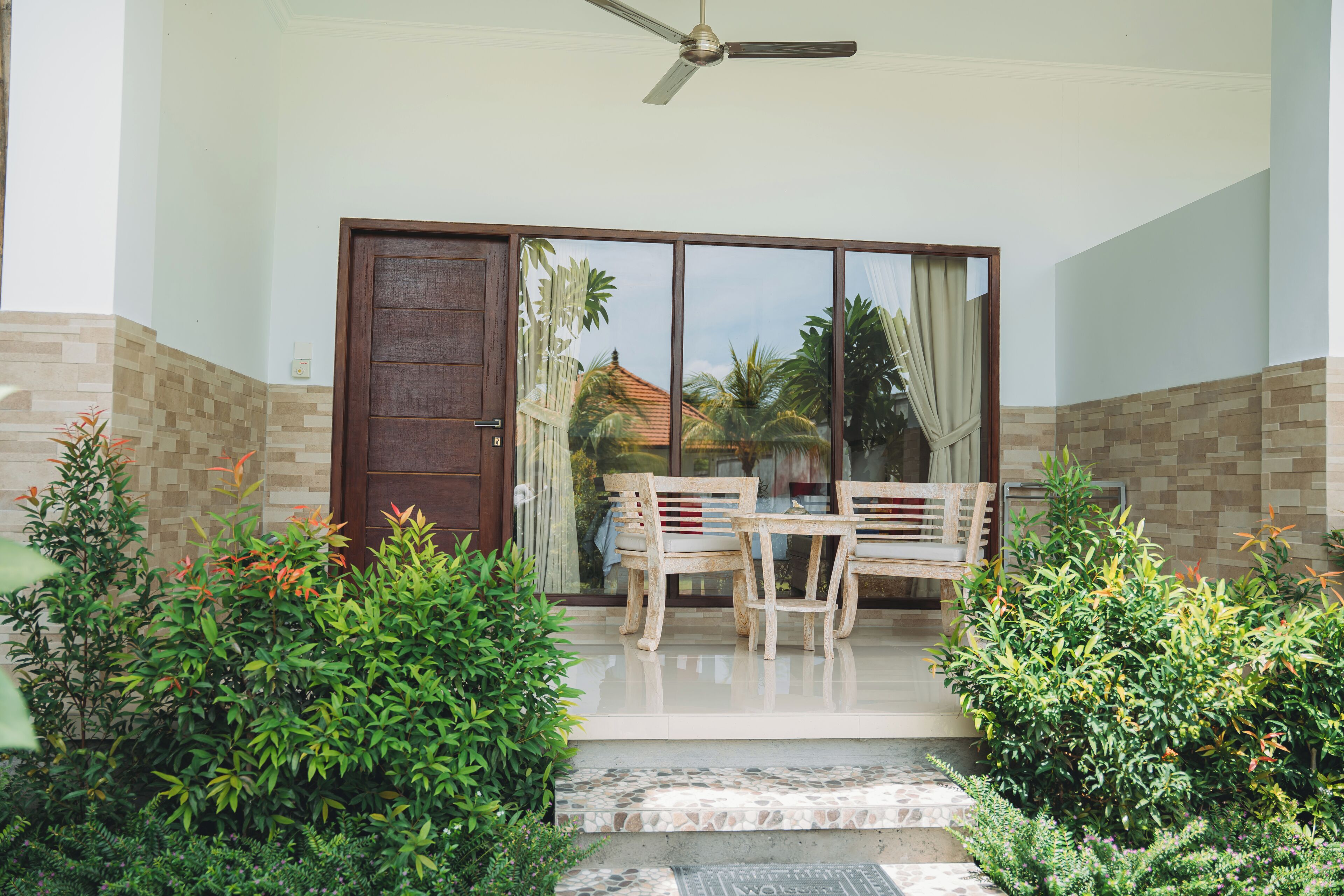 A covered outdoor seating area with a table and chairs, a sliding glass door, and a ceiling fan.