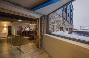 Interior de un hotel con piso de madera, una escalera y vistas a una montaña nevada a través de una ventana.