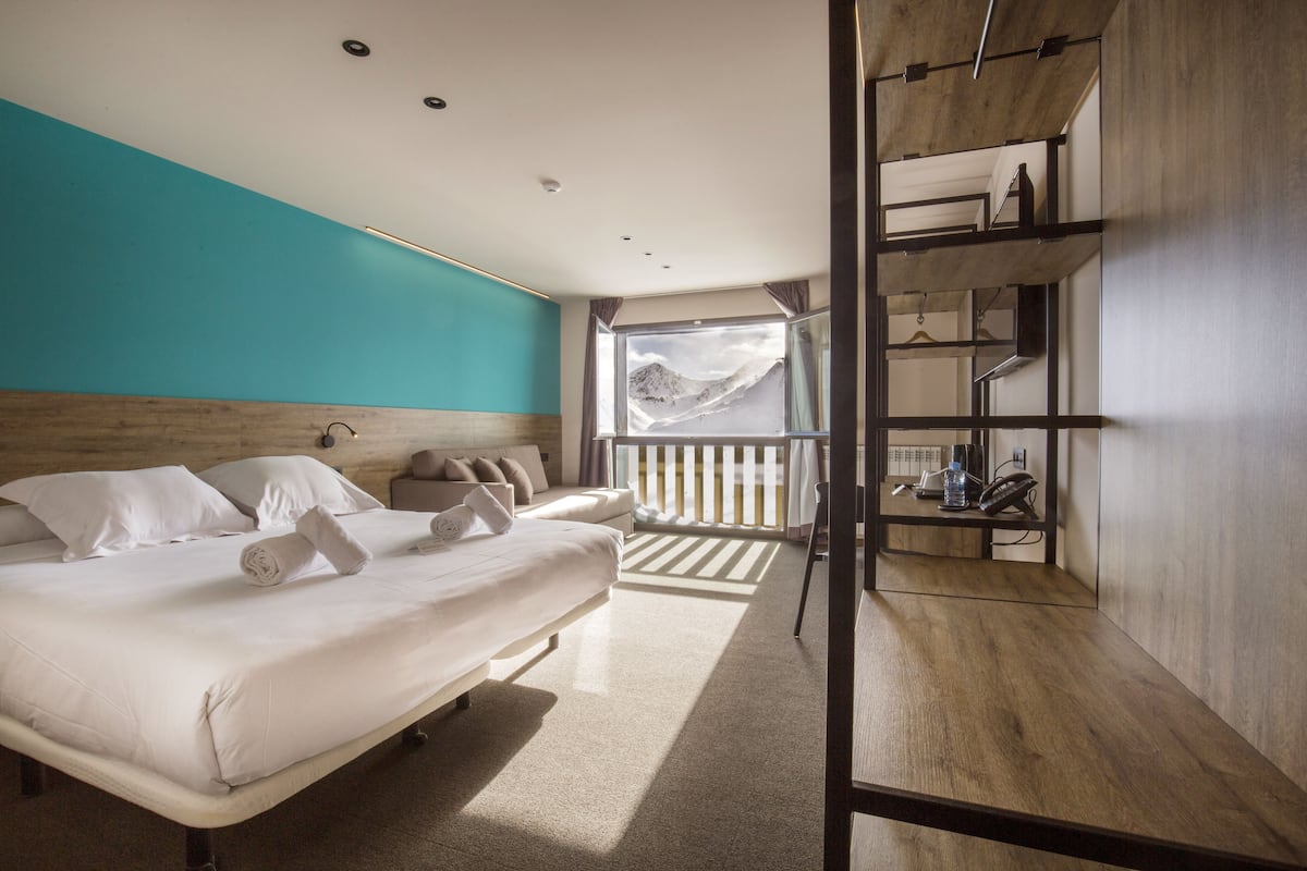 Une chambre d’hôtel moderne avec un grand lit, une vue sur les montagnes par la fenêtre et un décor intérieur en bois.