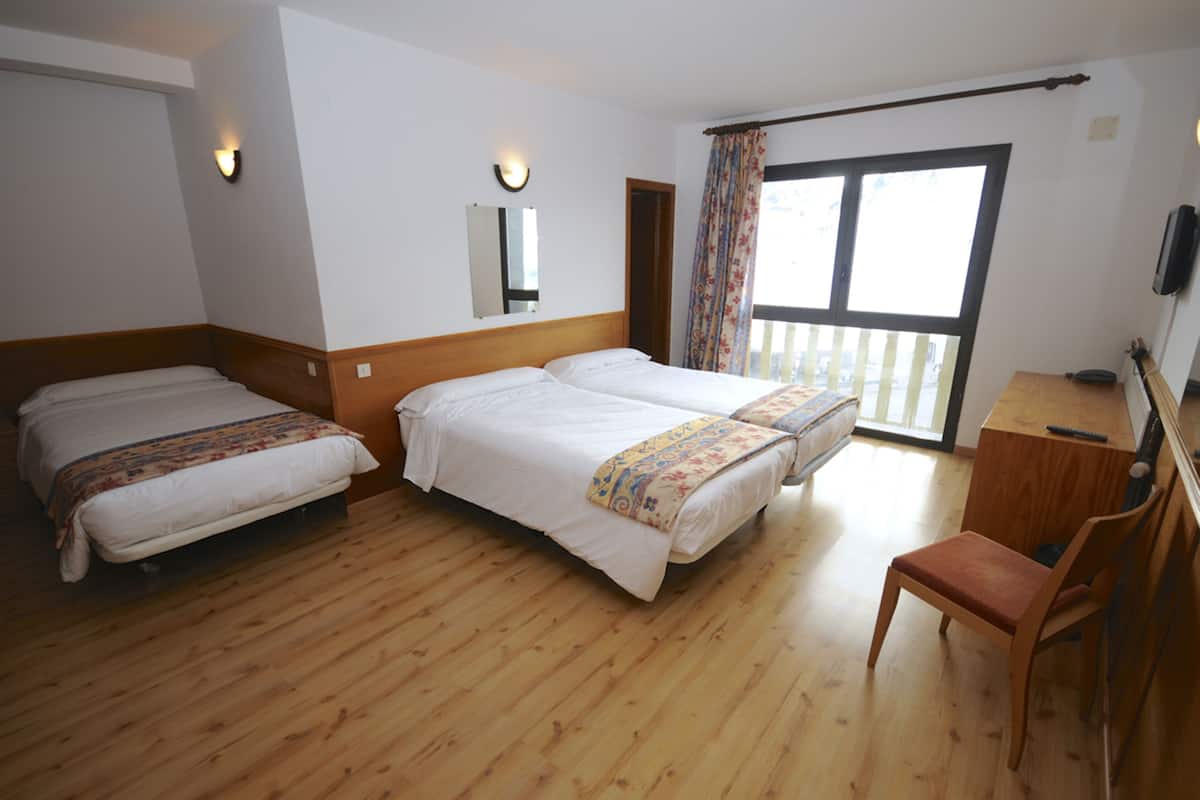 Une chambre d’hôtel avec deux lits simples, un bureau en bois, une chaise et une grande fenêtre avec des rideaux.
