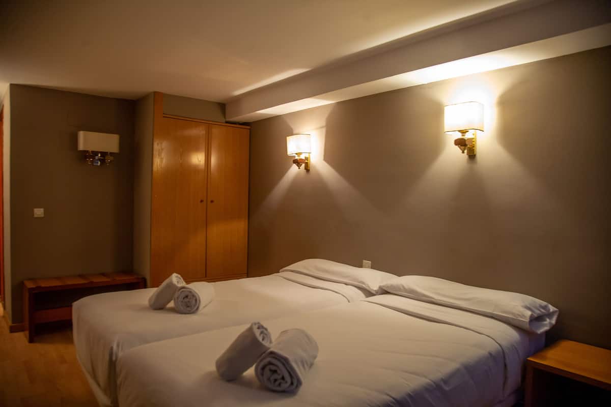 Une chambre d’hôtel avec deux lits, une armoire en bois et deux lampes fixées au mur.