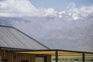 A modern building with a corrugated metal roof and wooden walls, set against a backdrop of snow-capped mountains and a clear sky. - La Morada Lodge - Valle de Uco (Tunuyan)