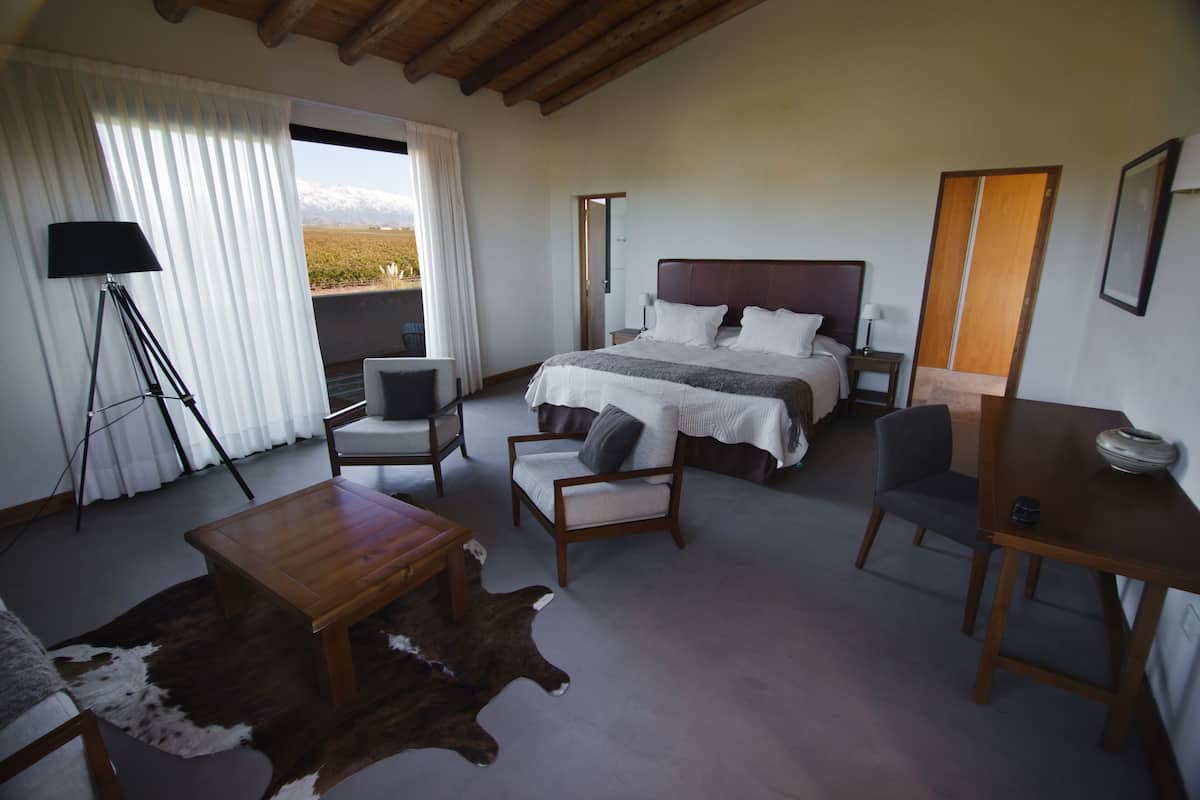 A bedroom with a large bed, two chairs, a small table, a lamp, and a view of the outdoors.