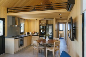 A modern kitchen with wooden cabinets, a dining area with a table and chairs, and a built-in oven. - La Morada Lodge - Valle de Uco (Tunuyan)