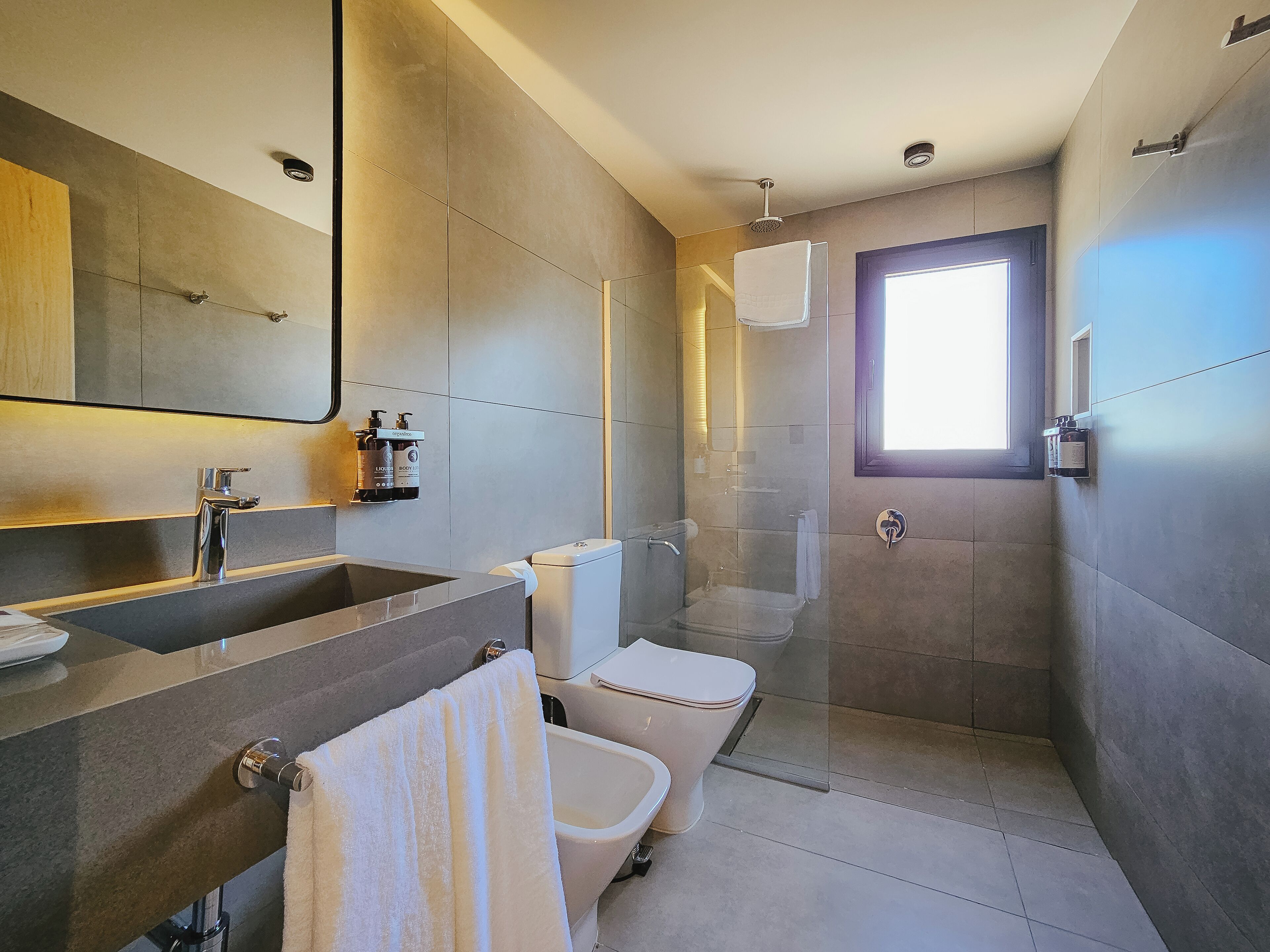 A modern bathroom with a large mirror, a sink, a toilet, and a shower enclosure.