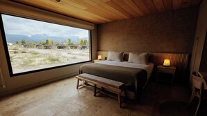 A bedroom with a large window, a bed, a bench, and a nightstand with a lamp. - La Morada Lodge - Valle de Uco (Tunuyan)