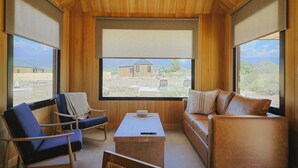A room with wooden walls and ceiling, large windows, a sofa, a chair, and a small table. - La Morada Lodge - Valle de Uco (Tunuyan)