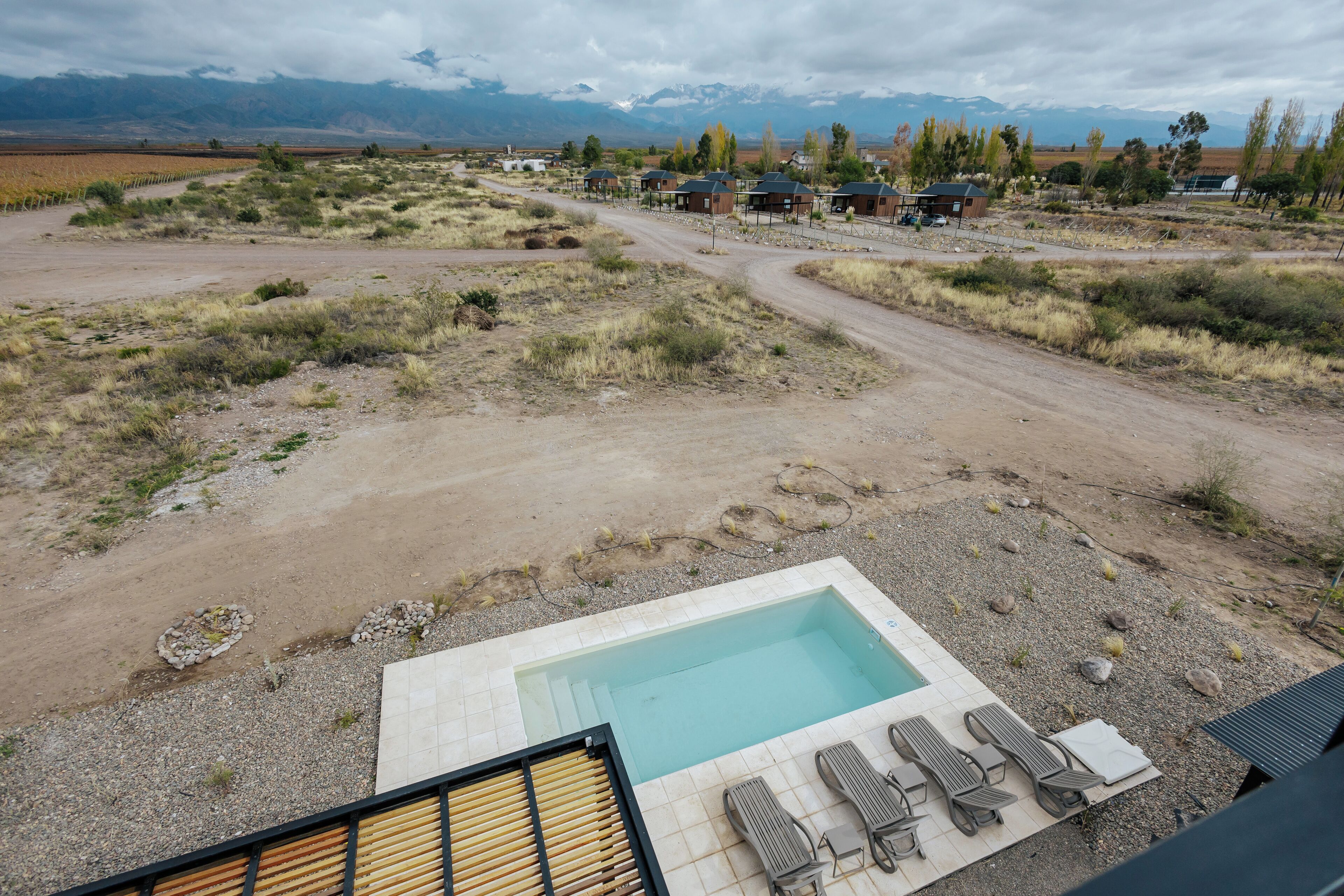 A pool area with lounge chairs, a view of a rural landscape with houses, and mountains in the background.