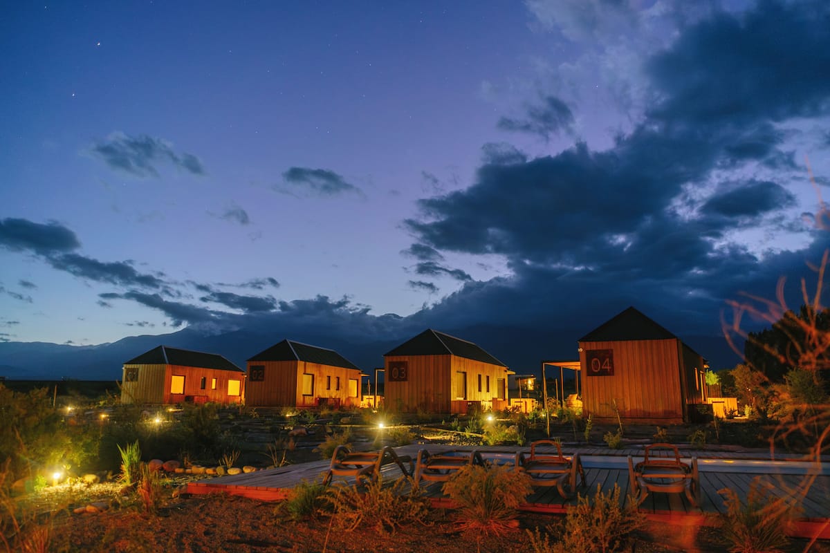 A row of wooden cabins with numbered doors, set against a twilight sky with clouds.