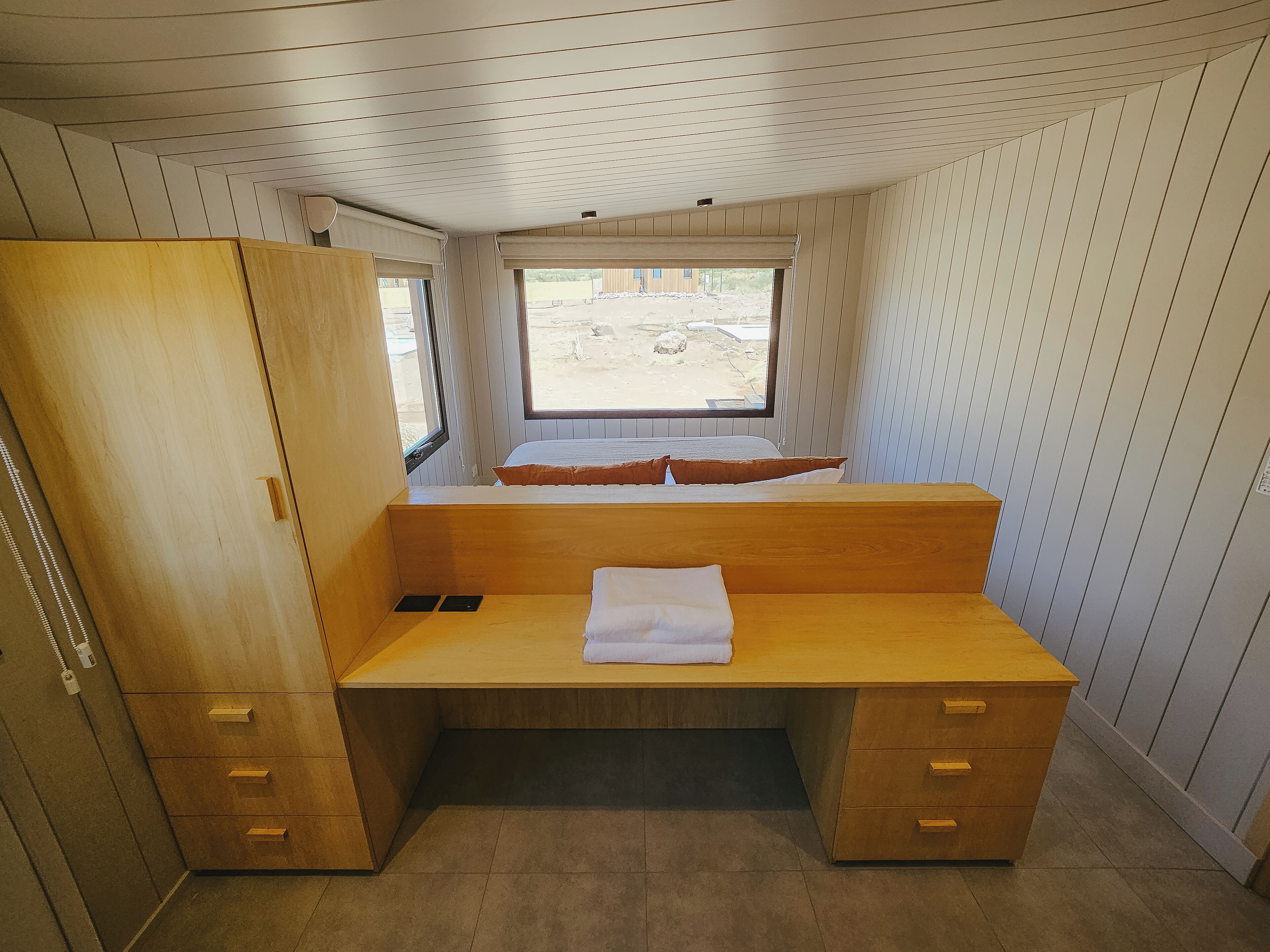 A compact room with a wooden desk, a bed with a window, and a wardrobe.