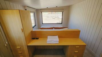 A compact room with a wooden desk, a bed with a window, and a wardrobe.