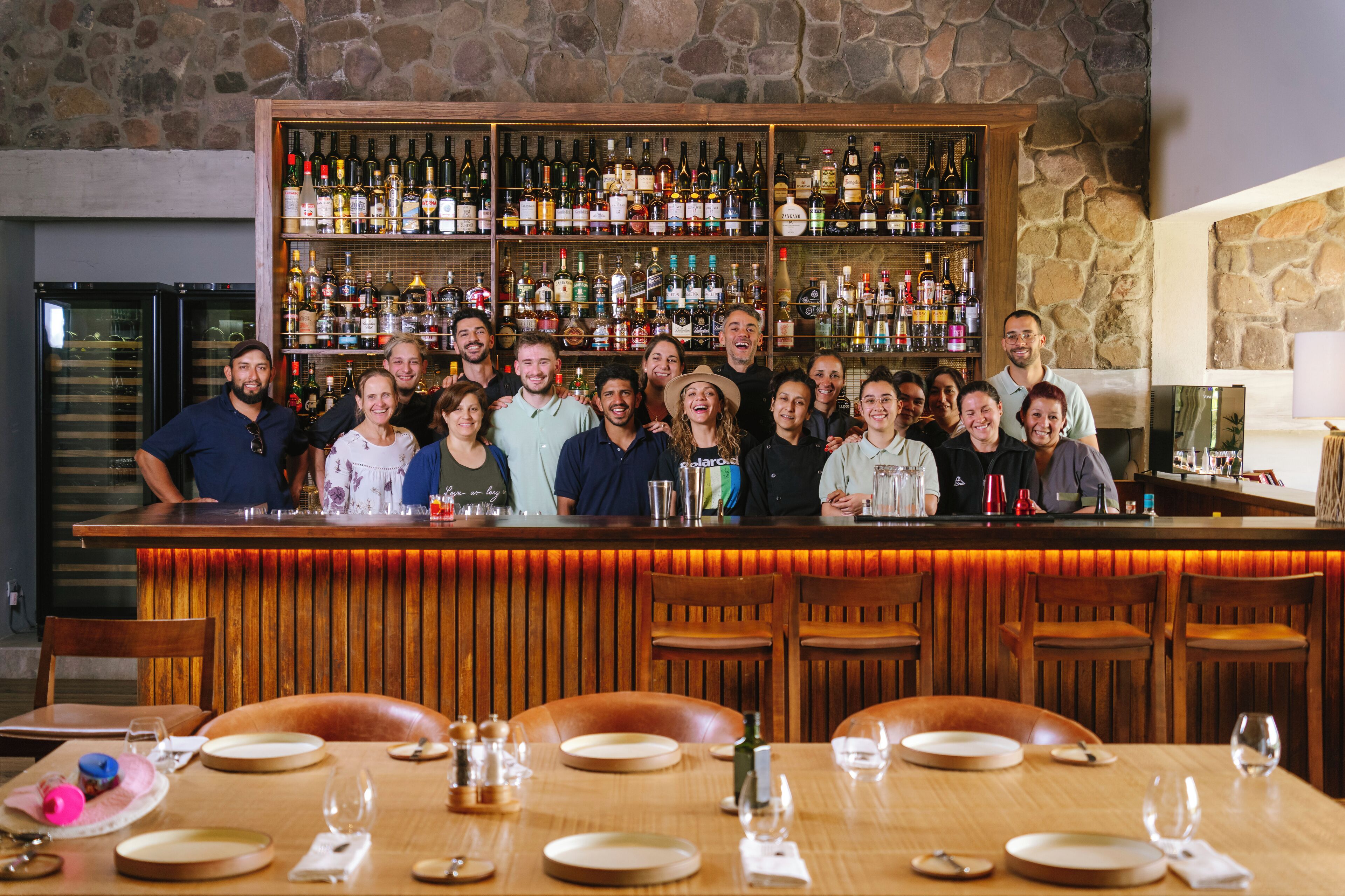 A bar area with a stone wall backdrop, wooden bar counter, and multiple seating arrangements.
