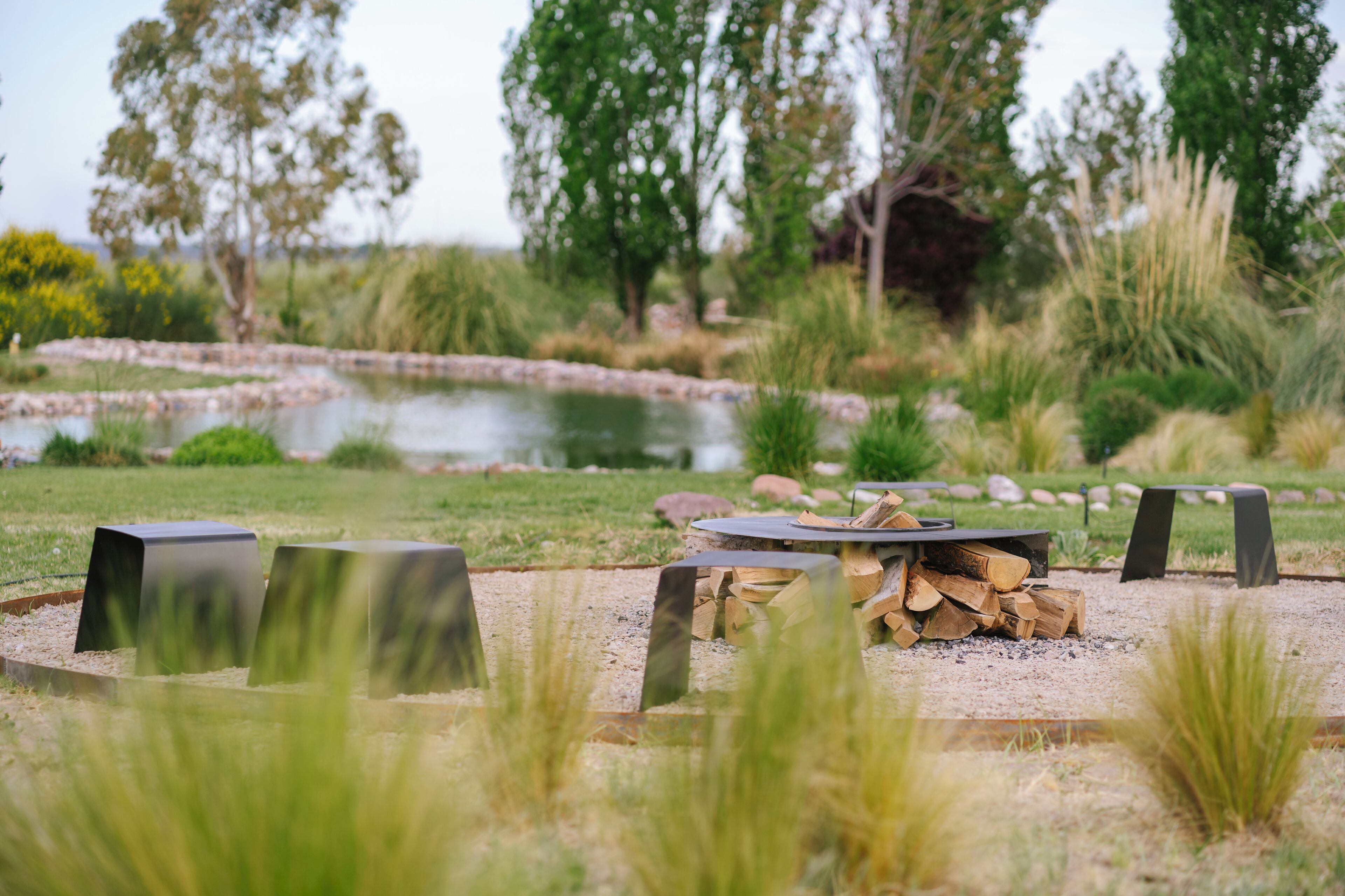Un espacio tranquilo al aire libre con una chimenea, rodeado de follaje natural y un estanque.