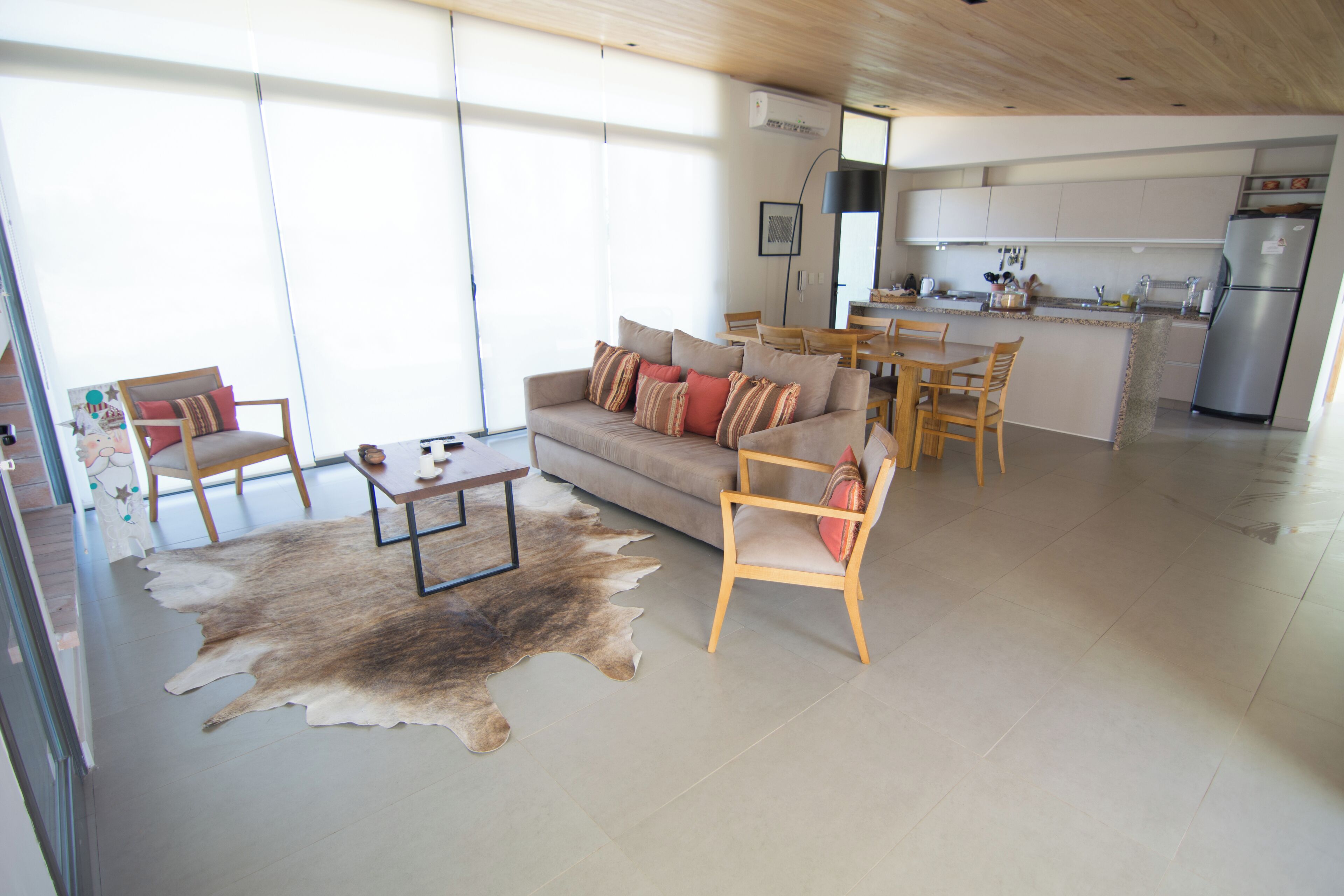 Un salon moderne avec un canapé, des fauteuils, une table basse et un coin repas, avec une cuisine en arrière-plan.