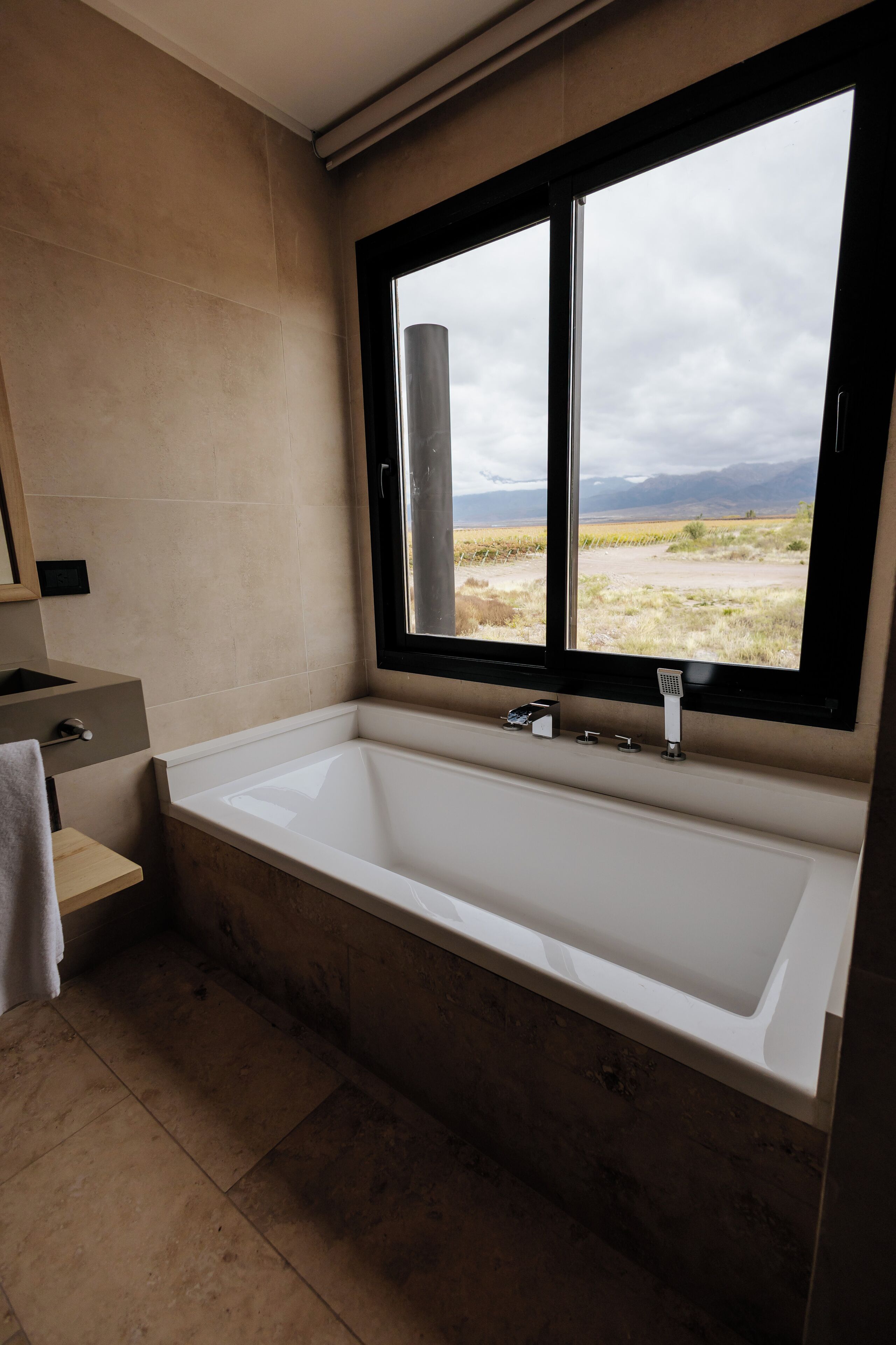 A modern bathroom with a large bathtub, a window with a view of a landscape, and a small vanity with a mirror.