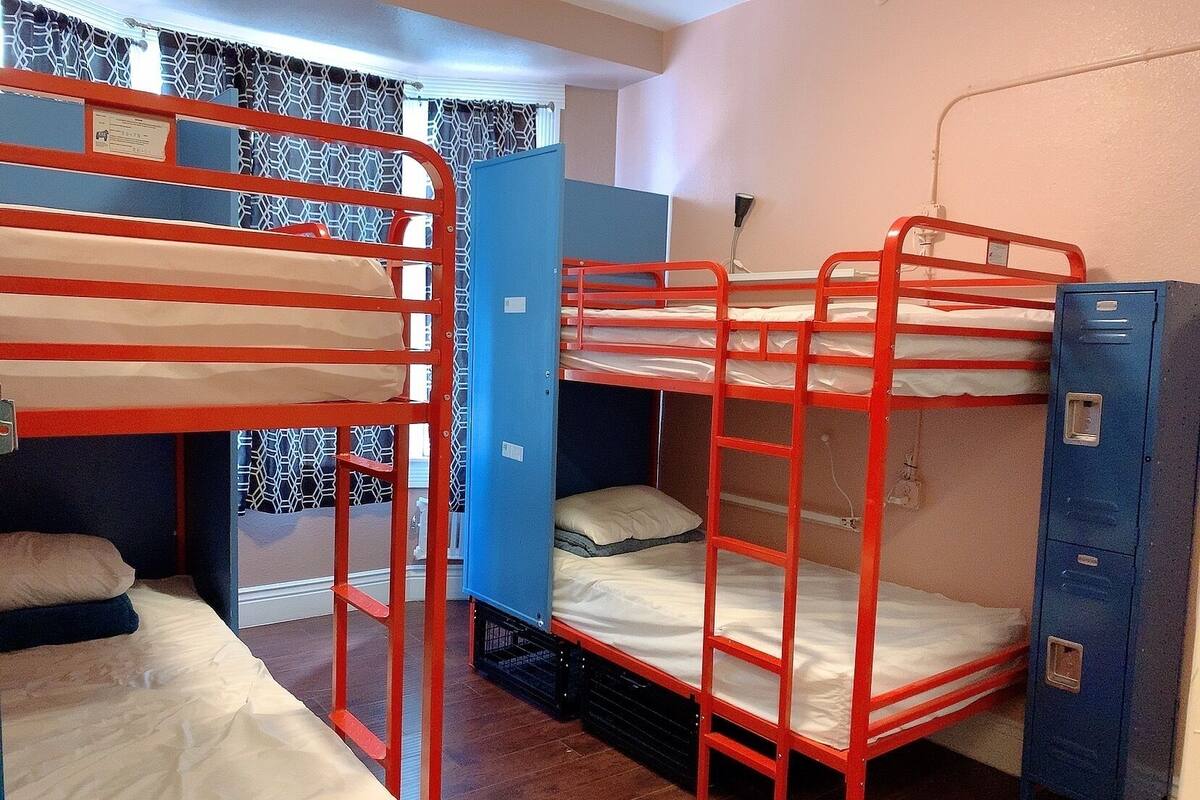 A dormitory room with bunk beds, a blue wardrobe, and a window with patterned curtains.