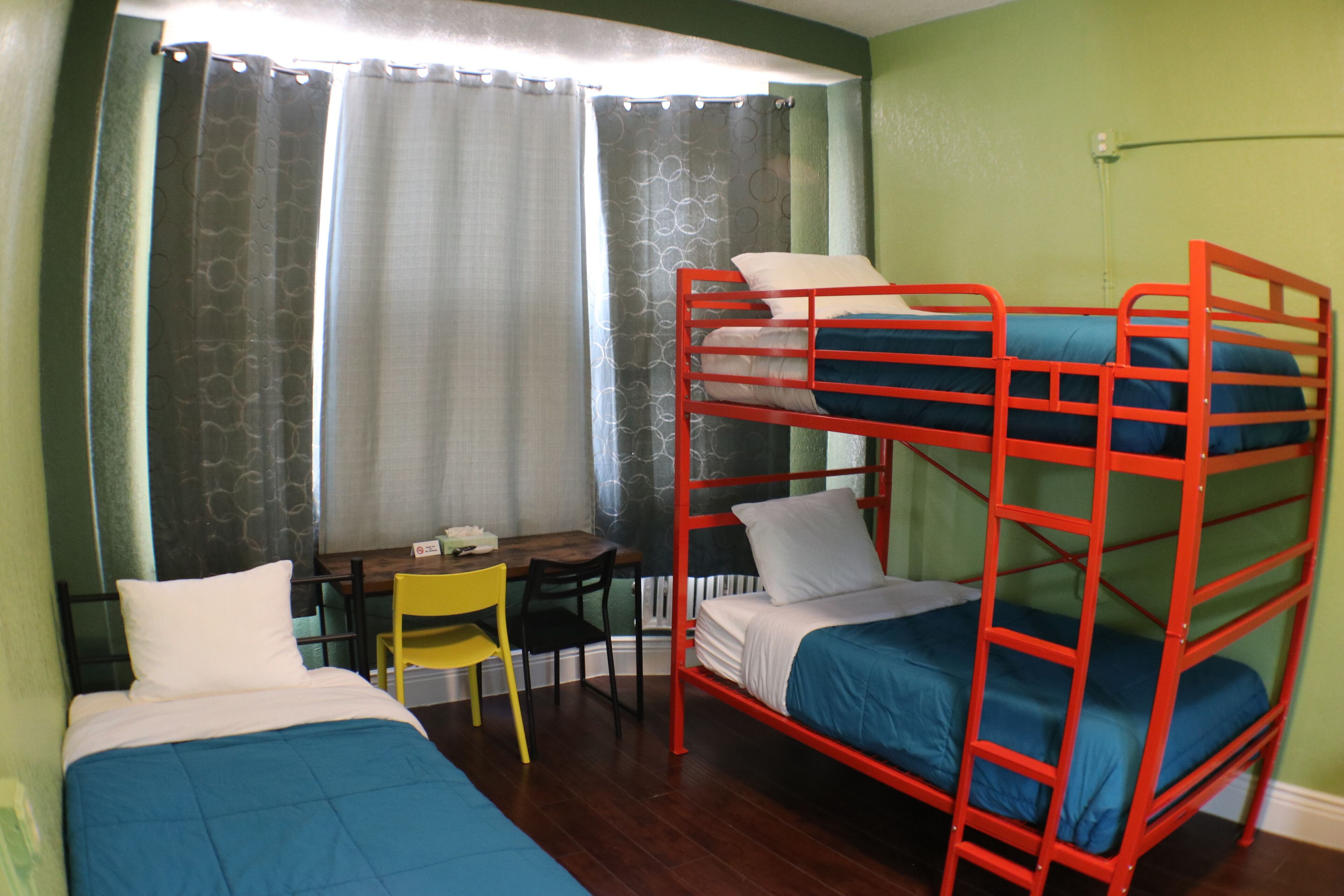 Habitación con literas, un escritorio, una silla, una ventana con cortinas y un radiador.