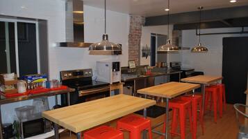 Une cuisine moderne avec des tables en bois, des tabourets rouges, des appareils en acier inoxydable et des luminaires suspendus.