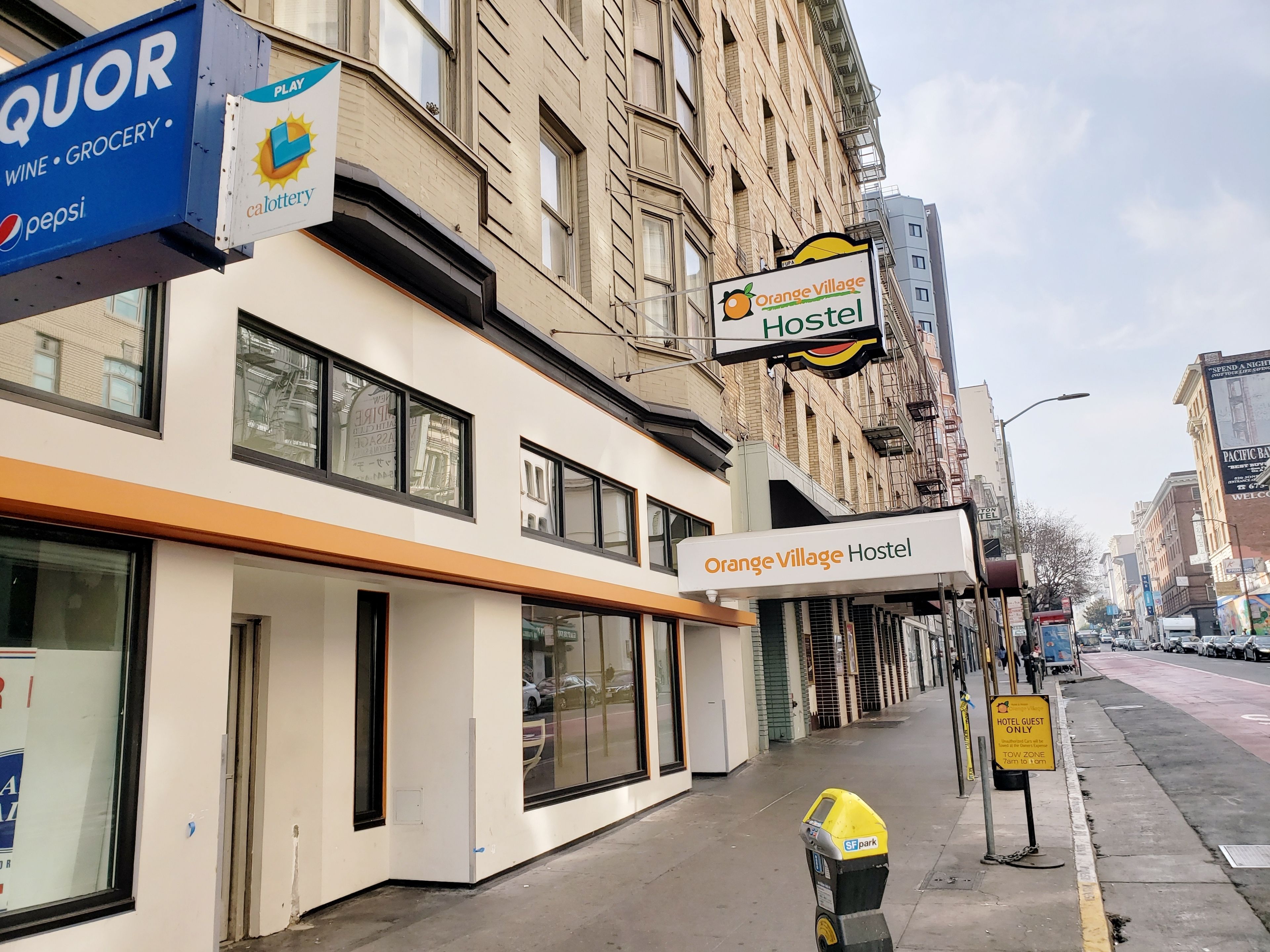 A street view with a building labeled "Orange Village Hostel" and a parking meter.