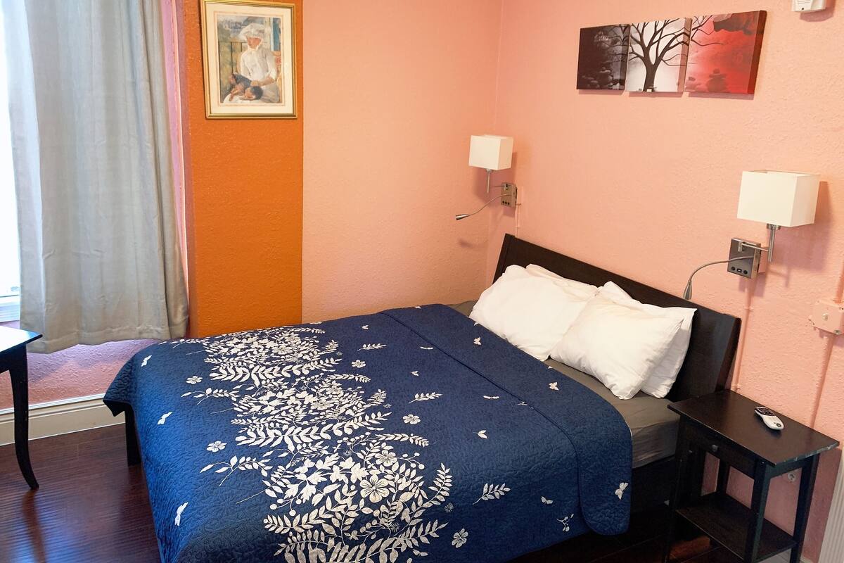 A bedroom with a bed, a nightstand, a lamp, and a painting on the wall.