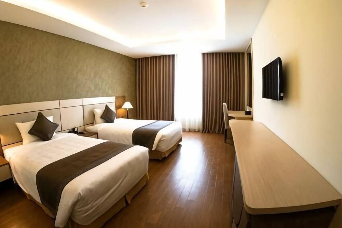 A hotel room with two beds, a desk, a TV, and a window with curtains.