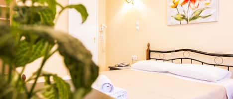 A hotel room with a bed, a bedside table, a wall-mounted lamp, and a painting of flowers.
