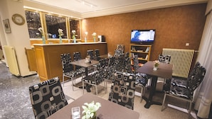 Comedor de hotel con televisor, varias mesas y sillas, y un mostrador de recepción.