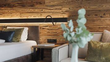 A modern hotel room with a wooden wall, a bed with multiple pillows, a bedside table with a book and glasses, and a small side table.