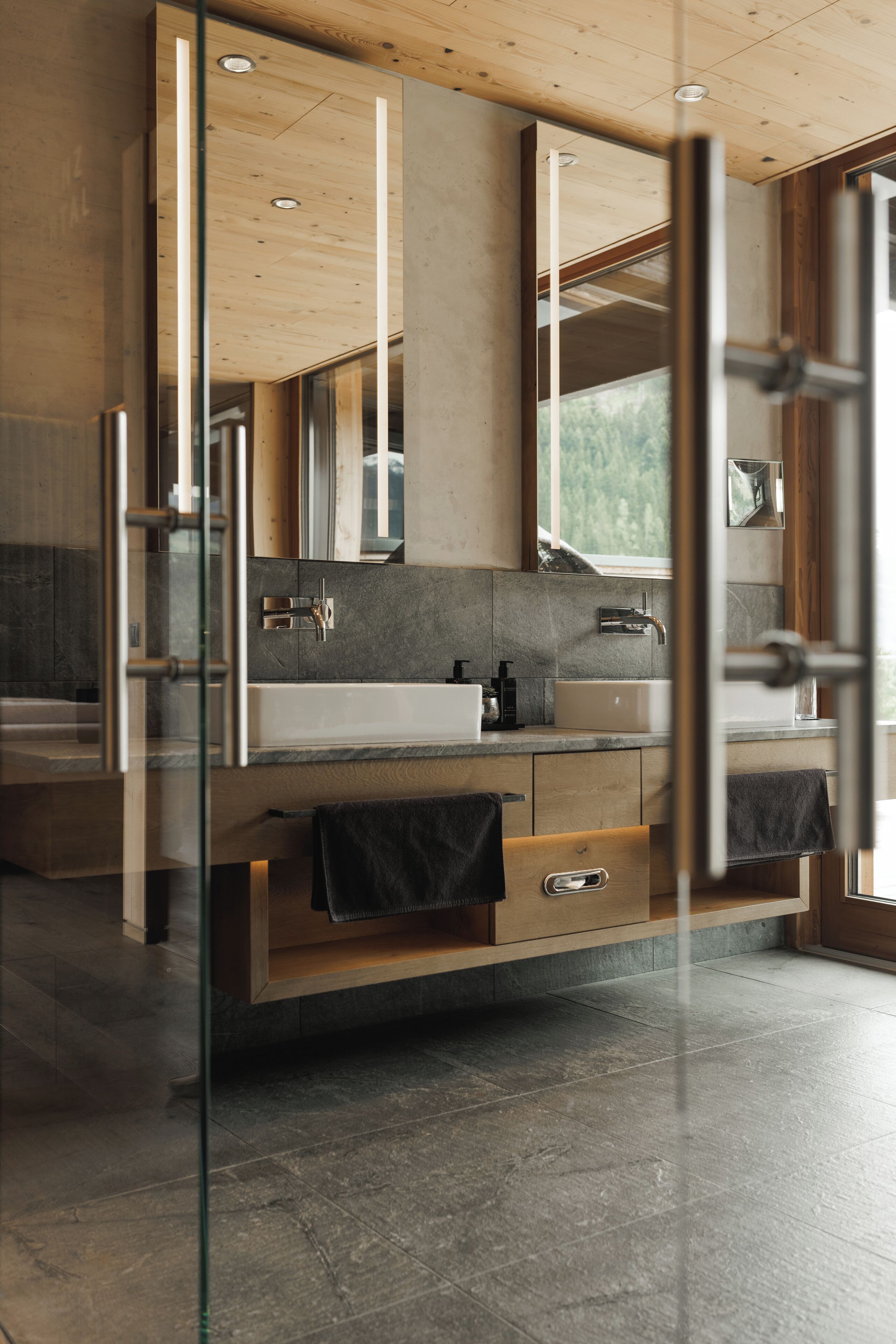 A modern bathroom with a glass partition, a large mirror, a white sink, and a wooden vanity.