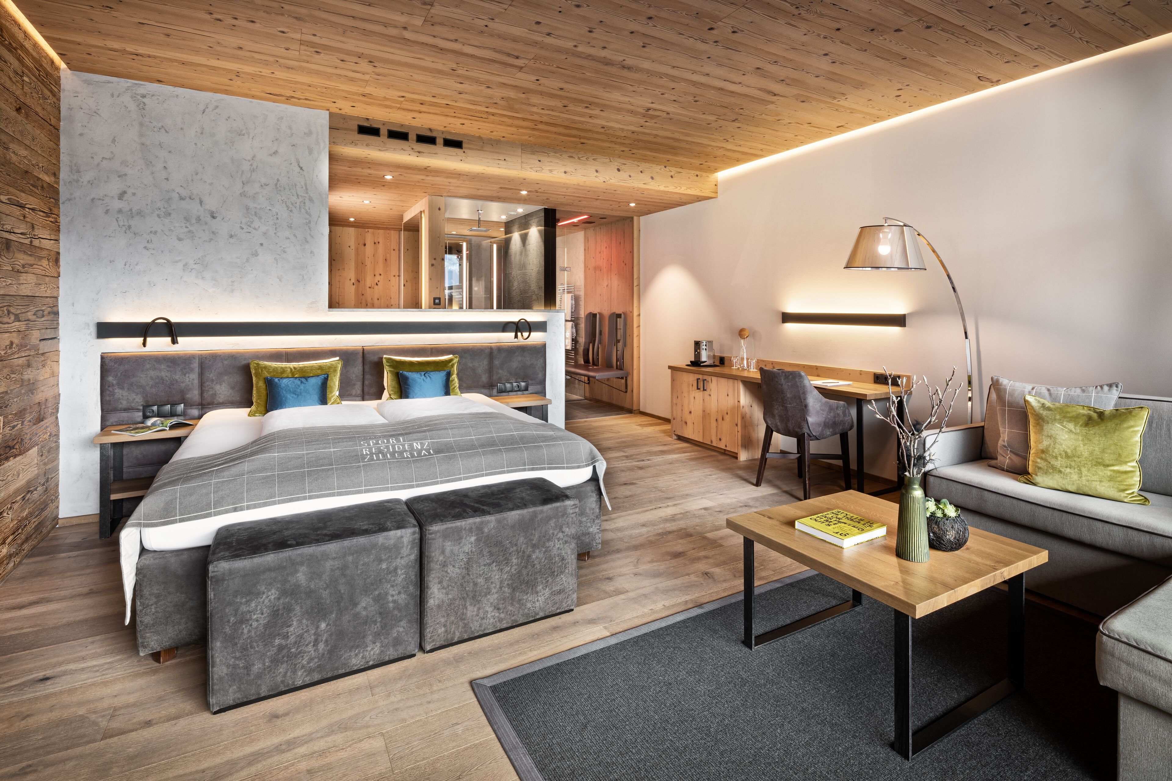 A modern hotel room with a large bed, a desk, a sofa, and a dining area.