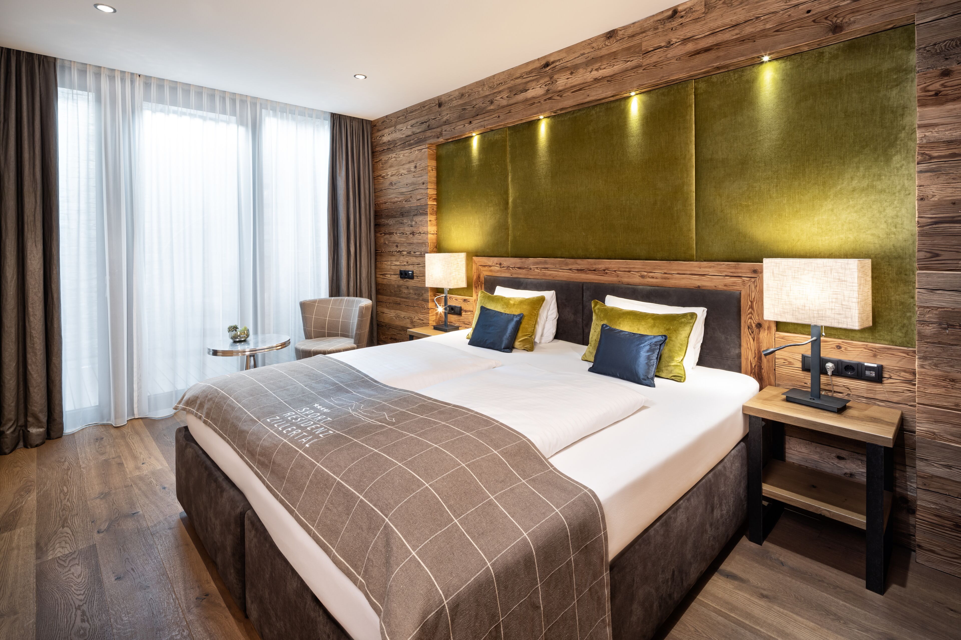 A hotel room with a large bed, two bedside tables, a chair, and a window with curtains.