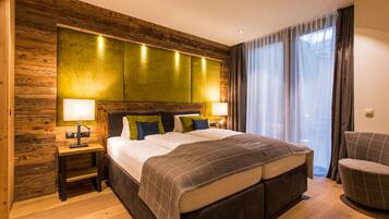 A modern hotel room with a large bed, wooden paneling on the walls, two bedside lamps, a chair, and a large window with curtains.