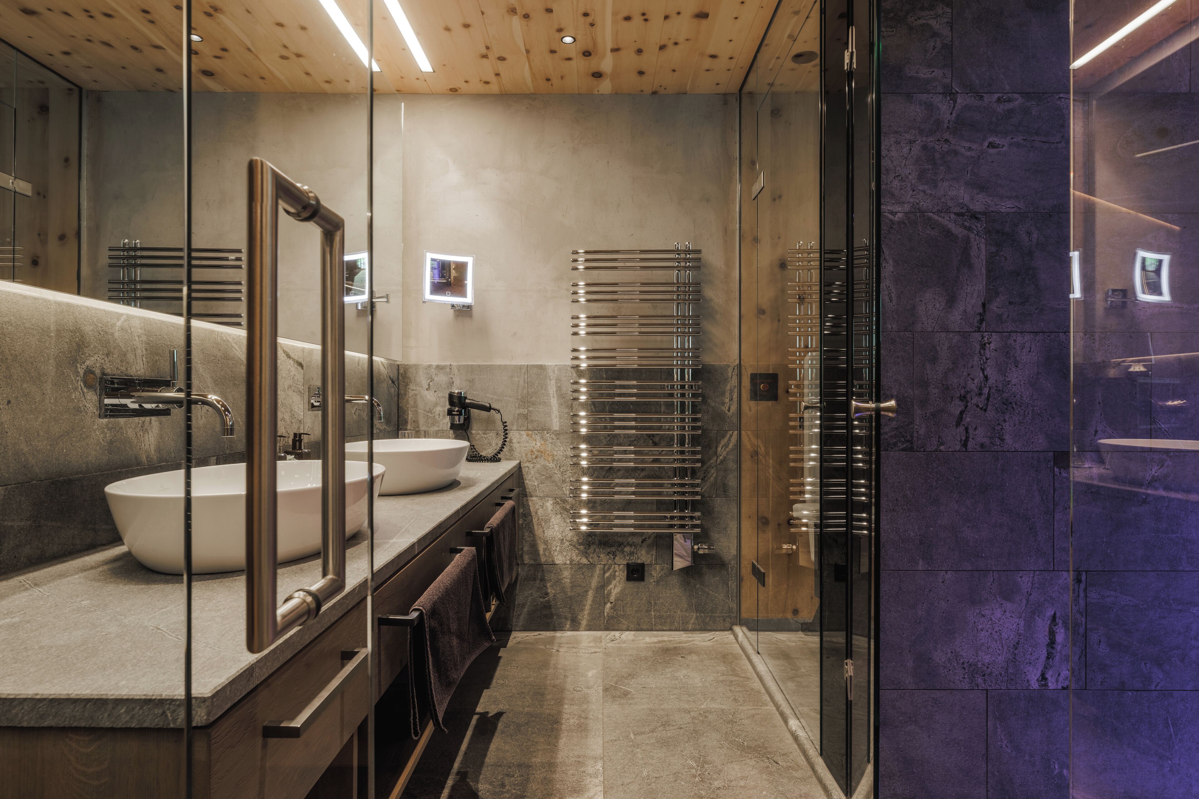 Une salle de bain moderne dotée d’un grand miroir, de deux vasques et d’une douche séparée par une paroi en verre.